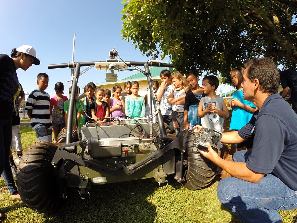 Rodrigo Romo (Right), PISCES project manager and robotics team lead, explains the nuts and bolts of the Helelani rover to Mahealani and her classmates.  