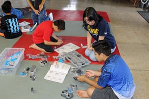 HawCC student Tayeh Madjeska leads Keaukaha students through the instruction manuals of a VEX IQ robotics kit.