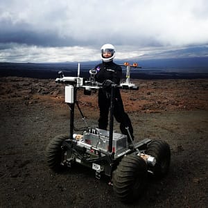 Right: Michaela Musilova, chief investigator for HI-SEAS, suited up for Mars and hitched a ride on the PISCES planetary rover last month as part of a film shoot at the habitat. HI-SEAS sits at roughly 8,000 feet above sea level on the rugged slope of Mauna Loa. PC: Musilova/HI-SEAS.